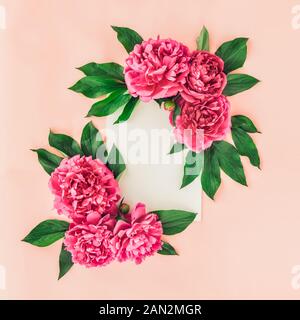 Delicate composition with empty vertical white blank canvas and pink peony flowers with green leaves on the warm pink background. Artwork mockup with Stock Photo