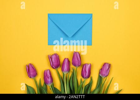 Pink, purple tulips and blue coral envelope on yellow background Stock Photo