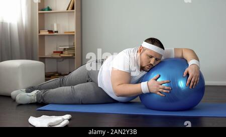 Tired unmotivated obese man lying on fitness ball, slimming fitness program Stock Photo