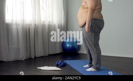 Fat belly man standing on fitness mat, preparing for morning gymnastic, sport Stock Photo