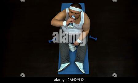 Sweaty obese man drinking water after sport training, restoring aqua balance Stock Photo