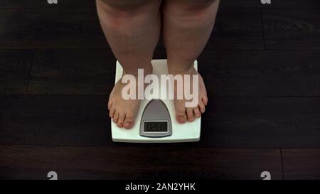 Fat man measuring weight on scales at home, obesity problem, sedentary life Stock Photo
