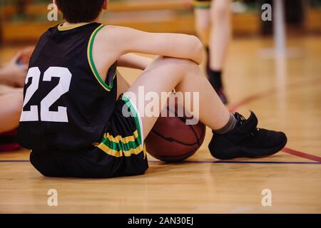 Junior basketball player sitting on the floor in backetball court Stock Photo