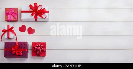 Gifts, backgrounds for Valentine's Day, Mother's Day. Multicolored gift boxes with red ribbons and hearts on a white wooden background with copy space Stock Photo