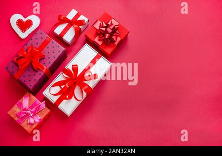 Gifts for Valentine's Day, Mother's Day. Multi-colored gift boxes with red ribbons and a handmade heart on a red background with copy space. Holidays. Stock Photo