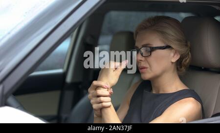 Attractive woman in eyeglasses sitting in car, suffering from wrist pain, health Stock Photo