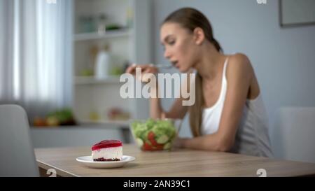 Slim woman eating healthy salad but dreaming about tasty cake, temptation Stock Photo