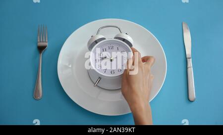 Daily regime, alarm clock on plate, adhere to diet time, proper nutrition Stock Photo