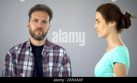 Sad man looking at camera, woman standing nearby, inability to discuss problems Stock Photo