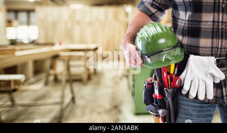 Close-up. Carpenter holds helmet and protective goggles in hand. Construction industry, carpentry workshop. Stock Photo