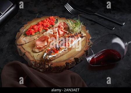 Brushetta set for wine. Variety of small sandwiches with prosciutto, tomatoes, parmesan cheese, fresh basil and balsamic creme served with glass of re Stock Photo