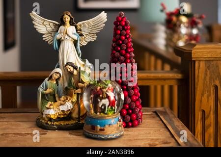 A Christmas nativity scene, a snow globe and a red miniature Christmas tree gathering on a rustic wooden table. Stock Photo