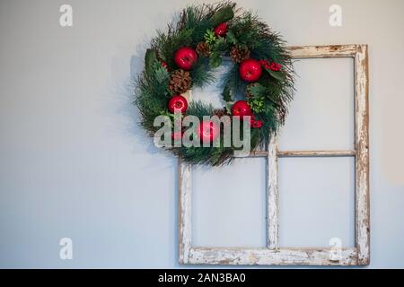 A red apple Christmas wreath hanging on an old vintage window frame, on the wall indoors. Stock Photo