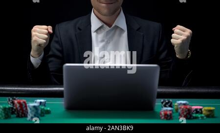 Gambler playing on laptop and showing success gesture, winning bet, fortune Stock Photo