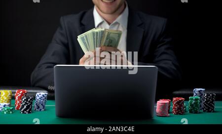 Successful online casino player counting money in front of laptop, bet winner Stock Photo