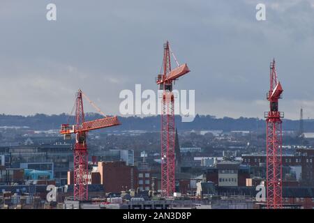 Three construction cranes set against a city skyline on a winters day Stock Photo