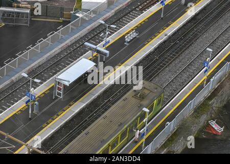 A birds eye view of a green train pulling into an empty station with two people taking cover from the rain Stock Photo