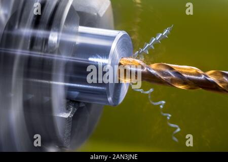 Rotating lathe detail. Screw drill bit cutting axial hole in metal workpiece. Artistic close-up of turning on shiny machine. Sharp drilling work tool.