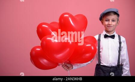 Little boy in vintage clothes with heart-shaped balloons smiling, Valentines day Stock Photo