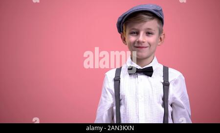 Funny little boy in vintage clothes smiling on camera against pink background Stock Photo