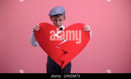 Little boy in vintage clothes trying to fix red broken toy heart unrequited love Stock Photo