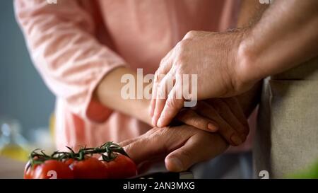 Elderly couple cooking traditional vegetarian meal and holding hands, family Stock Photo