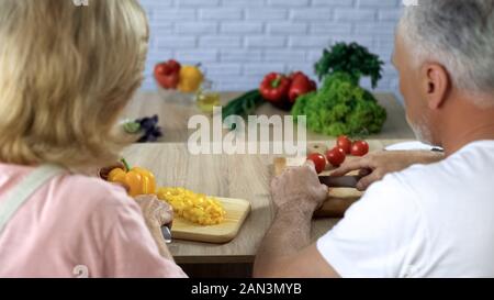Elderly married couple cutting vegetables in kitchen, cooking dinner together Stock Photo