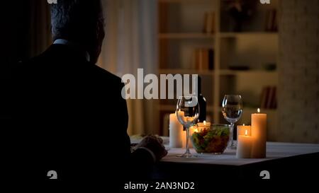 Aged man sitting at table served for romantic dinner, waiting woman, home date Stock Photo