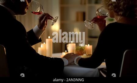 Elegant married couple drinking wine and holding hands, tender relations, spouse Stock Photo