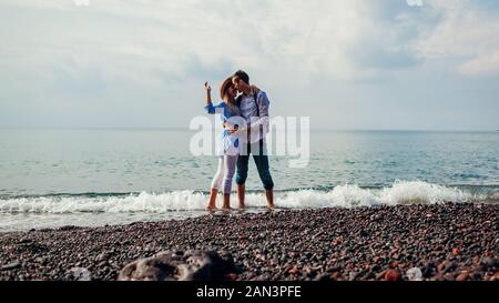 Valentines day. Couple in love kissing on honeymoon in Santorini island, Greece. People walking on beach by sea. Stock Photo