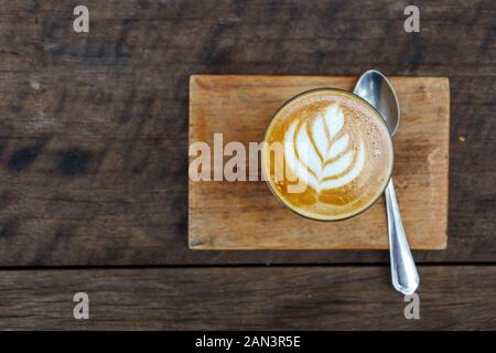 Top flat view one cup of cappuccino or latte with flower pattern of latte art in transparent glass on wooden tray and table. Stock Photo