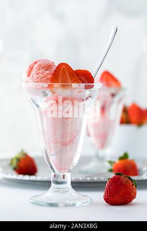 A front view of a strawberry ice cream sundae with another one on a metal tray in behind and a bowl of strawberries. Stock Photo