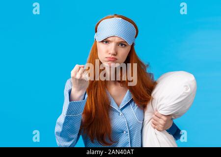 Who disturbed my sleep. Mad and displeased, angry grumpy redhead woman threaten sibling being too loud in morning, shaking fist frowning, holding Stock Photo