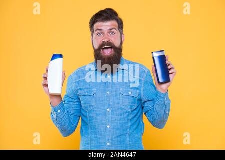 Grooming at every opportunity. Bearded man hold shampoo bottles yellow background. Cosmetics and toiletries. Hygiene and personal grooming. Male body grooming and skincare. Grooming products for men. Stock Photo