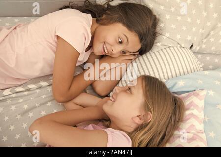 There is no friend than a sister. Happy little sisters talking during nap time. Small sisters relaxing in bed together. Adorable sisters or friends enjoying rest hour. Stock Photo