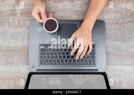 Hands holding a cup of coffee over laptop computer Stock Photo