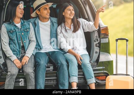 Asian man and women relaxing in back of car trunk during travel in summer. Transportation and people lifestyles concept. Group of happy friendship sit Stock Photo