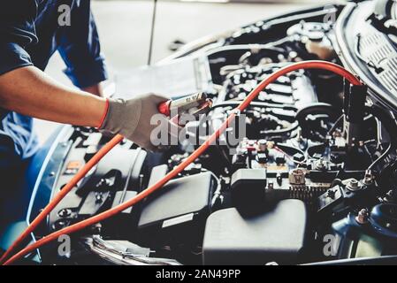 Car mechanic holding battery electricity trough cables jumper and checking to maintenance vehicle by customer claim order in auto repair shop garage. Stock Photo