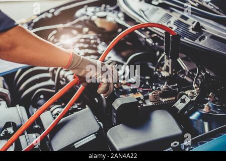 Car mechanic holding battery electricity trough cables jumper and checking to maintenance vehicle by customer claim order in auto repair shop garage. Stock Photo