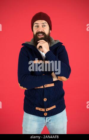 Warm and comfortable. Fashion menswear shop. Masculine clothes concept. Winter menswear. Clothes design. Man bearded warm jumper and hat red background. Winter season menswear. Personal stylist. Stock Photo