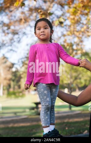 Little girl standing up on a platform and being supported by an adult for balance. Stock Photo
