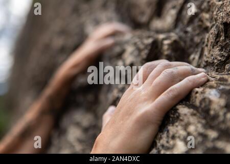 A closeup view of fingertips attempting to hold on to a limestone cliff, trying, failing and retrying to reach the top, not giving up conceptual shot Stock Photo