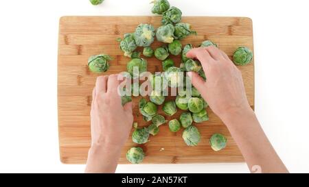 Brussels sprouts on a wooden cutting board, close up on white background, top view, woman hands Stock Photo