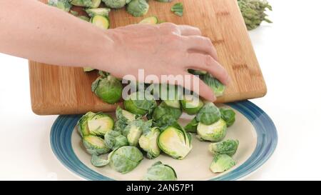 Brussels sprouts. Woman puts Brussels sprouts off cutting board on a plate, close up on white background Stock Photo