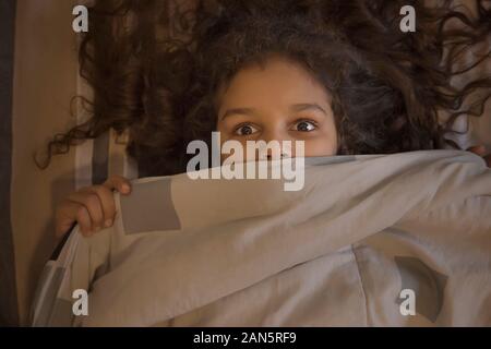 Young girl looking out surprisingly from under the blanket. (Children) Stock Photo