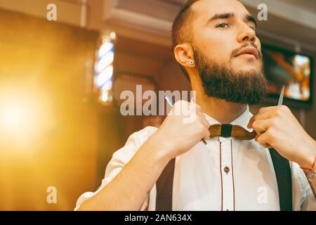 Young handsome bearded barber straightens his bow-tie. Copy space. Barber shop Stock Photo