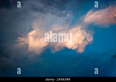 Unusual white cumulus clouds in the blue sky at sunset time. Natural background for design. Stock Photo