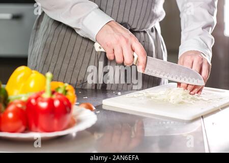 Closeup of hand with knife cutting fresh vegetable. Young chef cutting beet on a white cutting board closeup. Cooking in a restaurant kitchen Stock Photo
