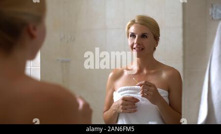 Smiling woman holding cotton swab at bathroom, everyday hygiene, cleaning ears Stock Photo