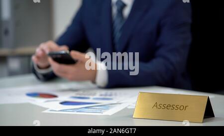 Male assessor in business suit using smartphone, working on important documents Stock Photo